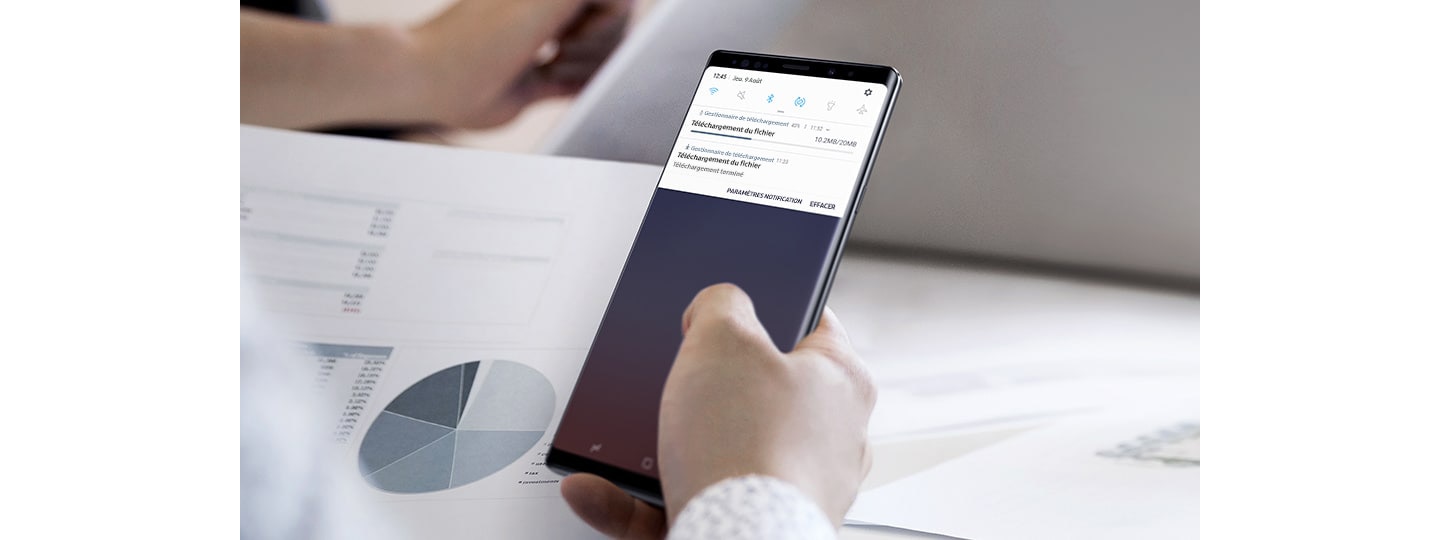 Image d’une personne tenant un Galaxy Note 9 avec l’interface utilisateur graphique (GUI) de téléchargement à l’écran, un téléchargement en cours et un autre terminé