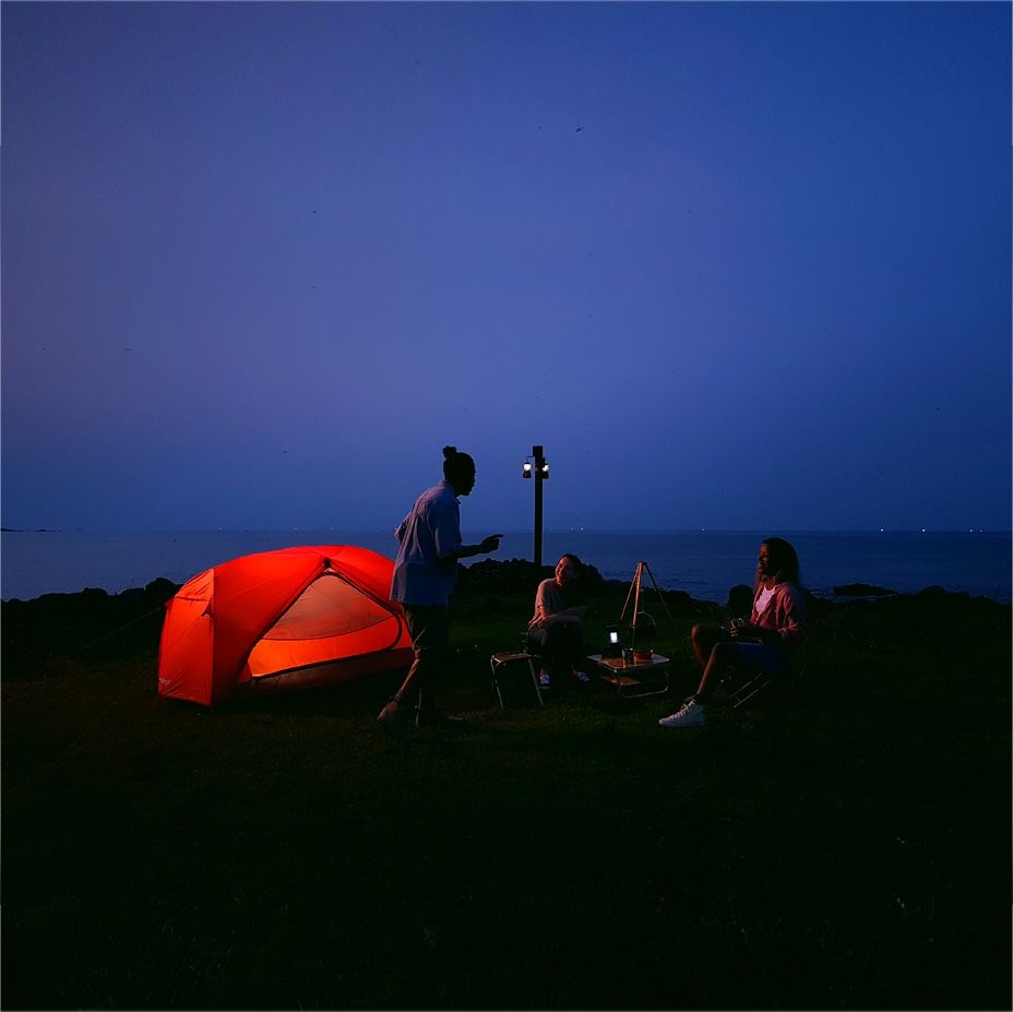 Sur l'écran du Galaxy Note8, on voit une photo prise par un Galaxy Note8 montrant des amis en train de camper la nuit à côté d'une tente rouge.