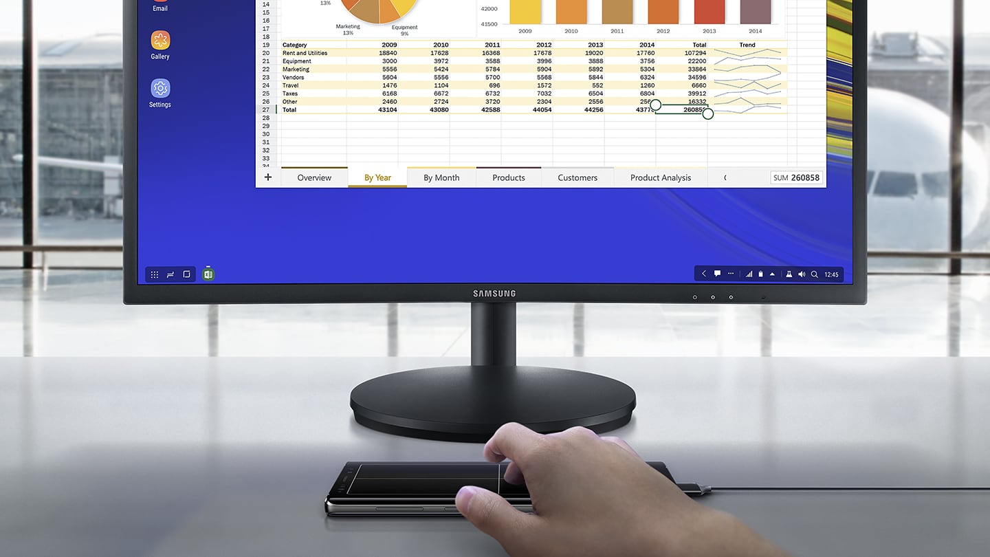 Imitacinis vaizdas su žmogumi, kuris naudojasi prie „Samsung DeX“ vienu laidu prijungtu „Galaxy Note9“, žiūri į ekrano skaičiuoklę prijungtame monitoriuje ir naudojasi „Galaxy Note9“ kaip jutikline planšete