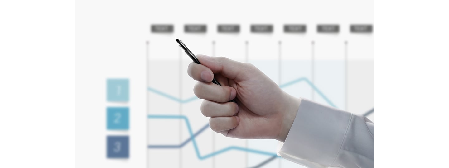 Simulated image of a person holding the S Pen with a presentation in the back showing a line graph. After the person clicks the S Pen button, the presentation slide switches to another graph.