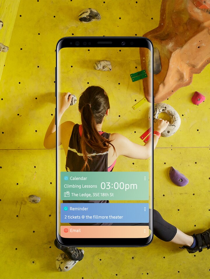 Seorang wanita pemanjat tebing indoor dan tampilan depan Galaxy S9 Midnight Black menampilkan aplikasi yang diatur di Bixby Beranda.