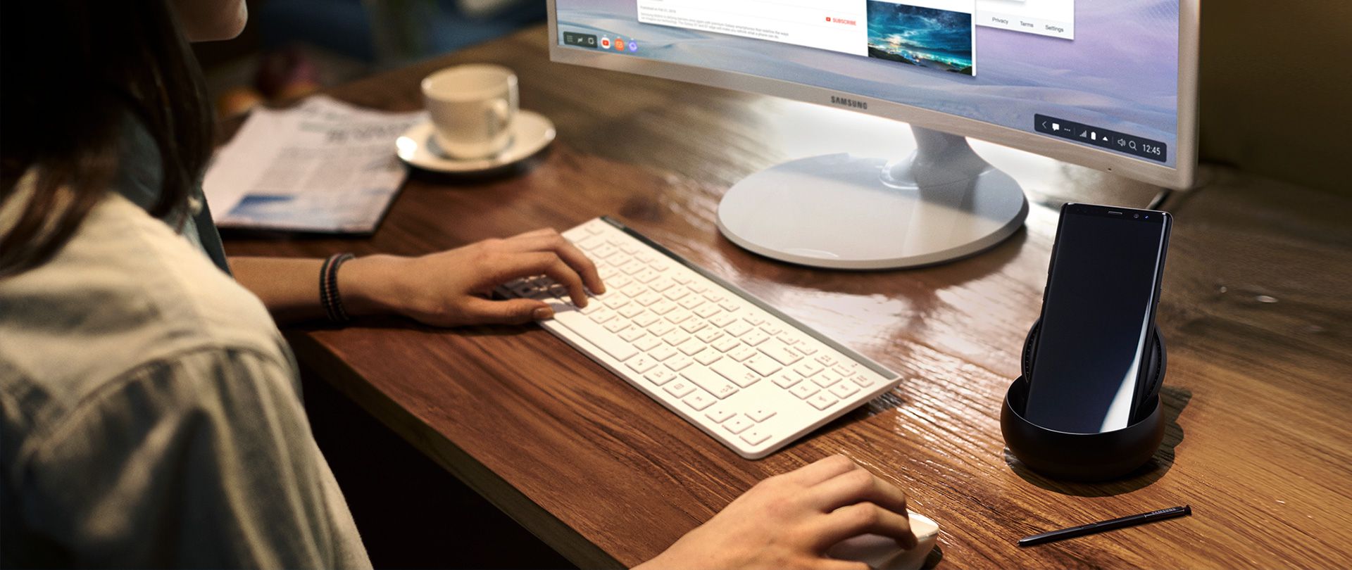Image of a person using Galaxy Note8 and DeX Station at a desk with a Samsung monitor, keyboard, and mouse