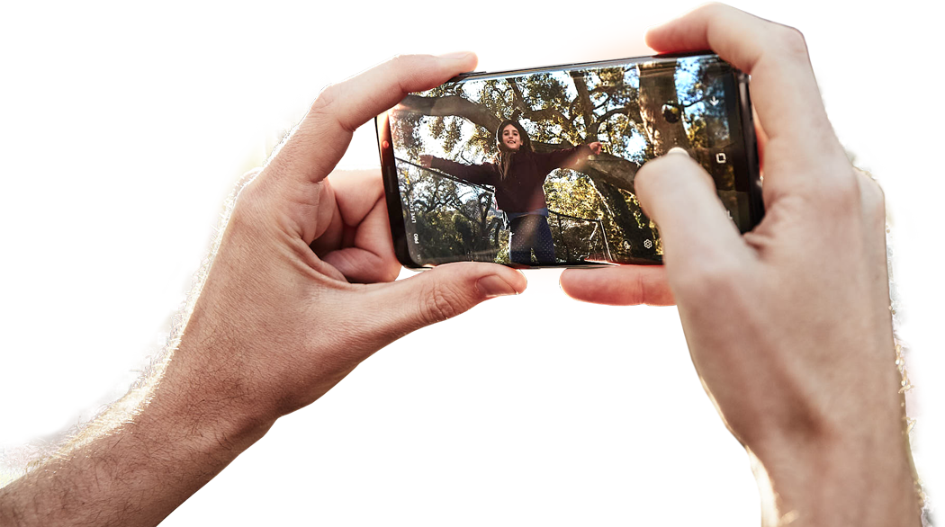 Image of a person taking a photo with Galaxy S9 with a photo displayed on-screen and the scene shown in the background to demonstrate OIS
