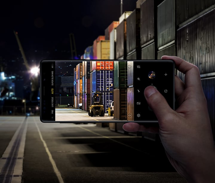 Imagem da pessoa a segurar o Galaxy Note9 e a tirar uma foto de contentores num depósito, demonstrando o Otimizador de Cenas