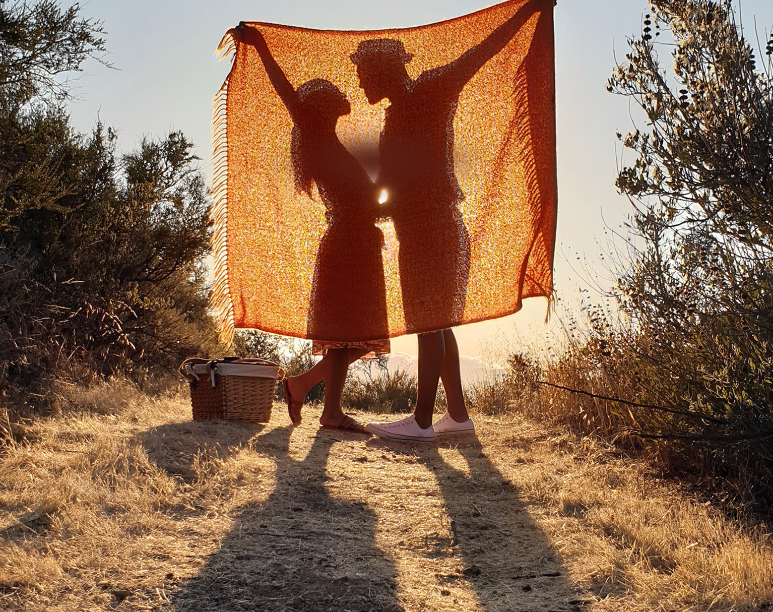 A photo taken by Galaxy Note9 of two people standing in a field behind a blanket with their shadows illuminated by the sun behind them