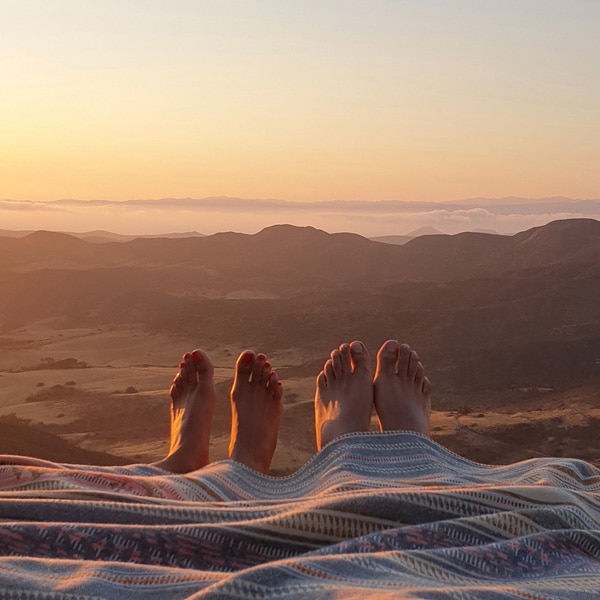A photo taken by Galaxy Note9 of two pairs of feet peeking out from under a blanket in the sunset, appearing to hang off a cliff