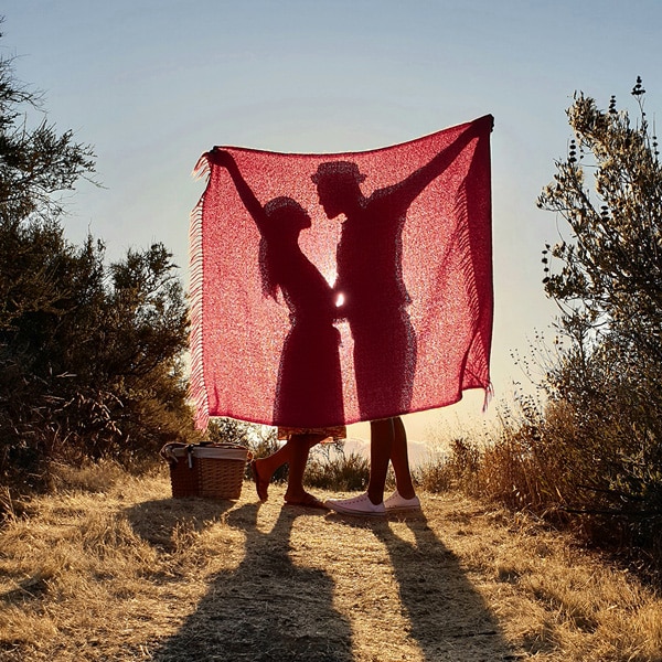 A photo taken by Galaxy Note9 of two people standing in a field behind a blanket with their shadows illuminated by the sun behind them