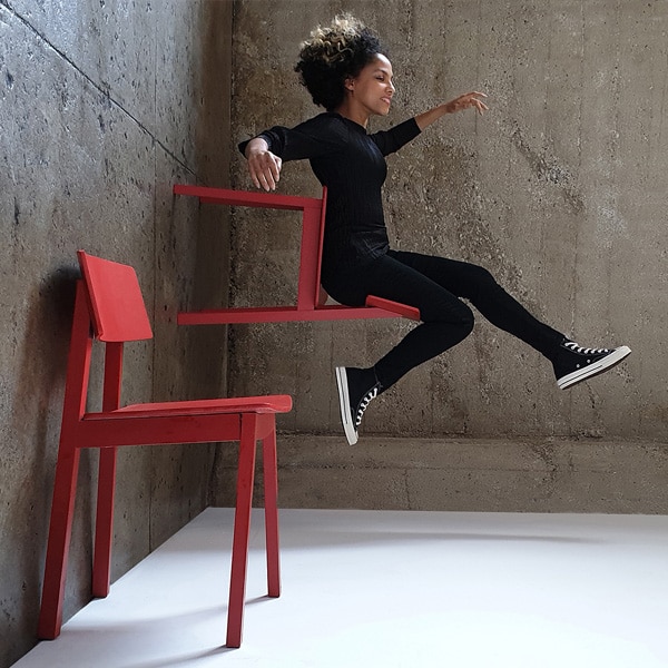 A photo taken by Galaxy Note9 of a woman wearing all black, sitting in a red chair that appears to be standing on the wall