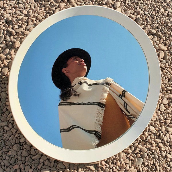 A photo taken by Galaxy Note9 of a person wearing a black hat, reflected in a mirror that’s sitting on stones