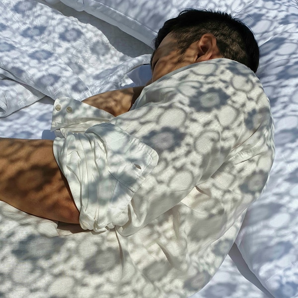 A photo taken by Galaxy Note9 of a man wearing a white shirt, laying on white sheets, with a lace shadow pattern cast on him